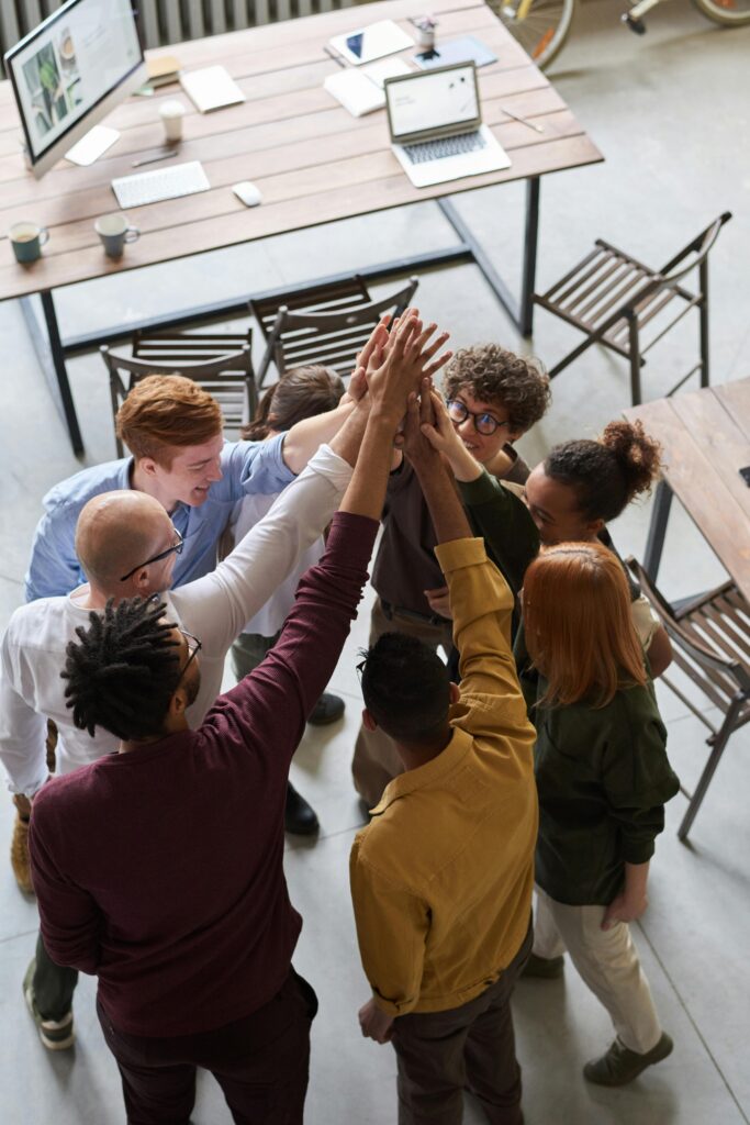 A diverse group of professionals high-fiving in a modern office, showcasing teamwork and collaboration.